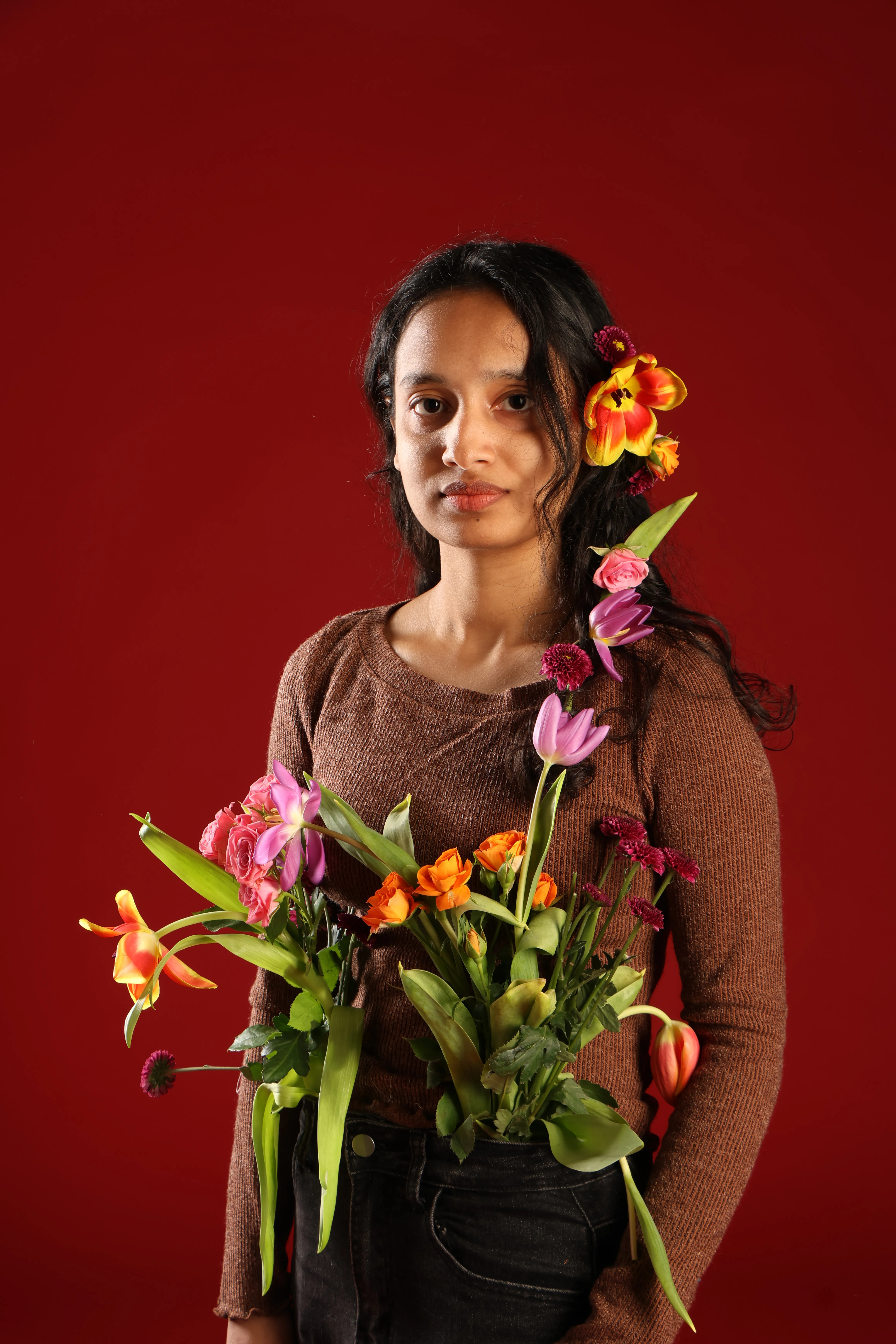 Rownok Jahan Tithi — fashion designer, holding a bouquet against a deep crimson studio backdrop